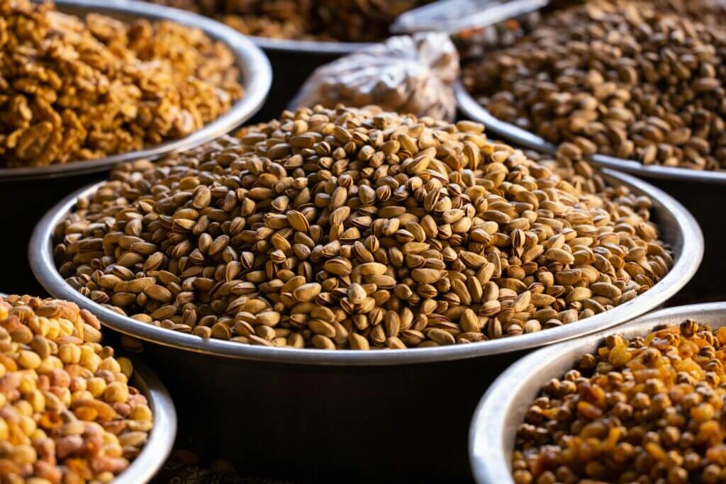 Close-up of assorted nuts and seeds displayed in metal bowls at a market setting.