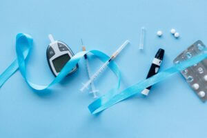 Flat lay of diabetes management tools with blue ribbon symbolizing awareness on a light blue background.