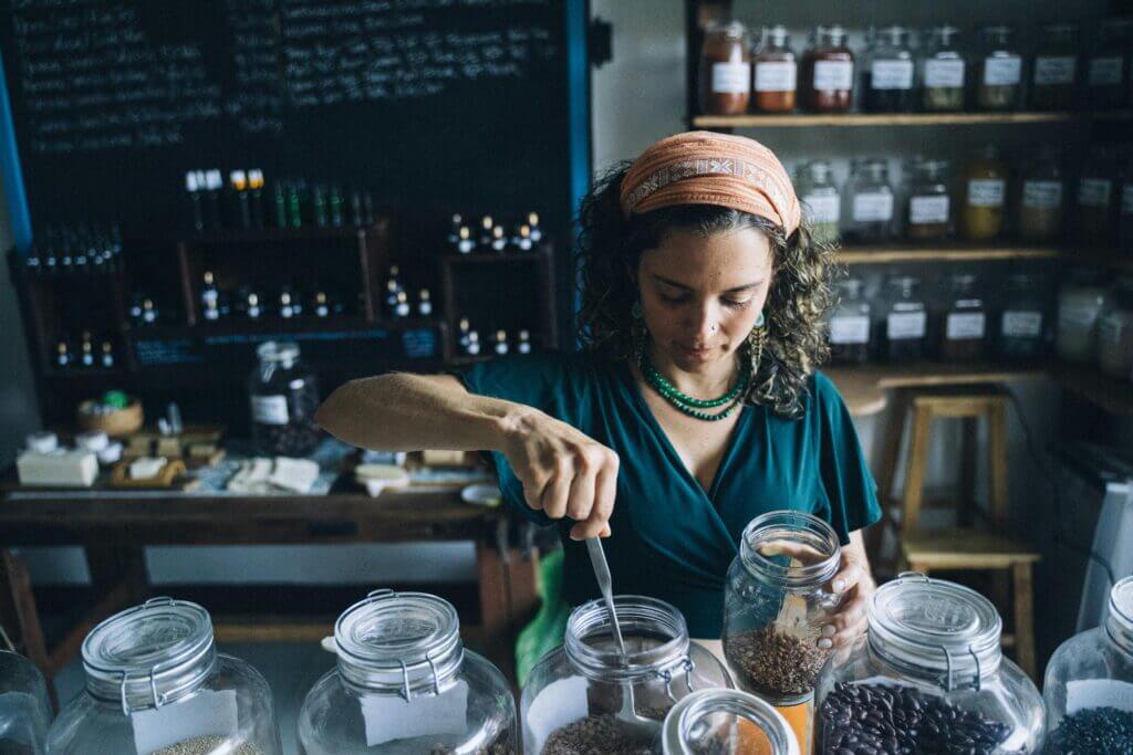 Woman in eco-friendly store preparing organic products using glass jars with a variety of ingredients.